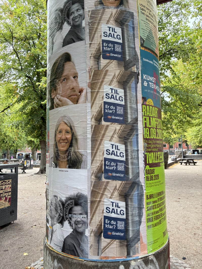 En plakatsøjle under træer med Låneklars plakater