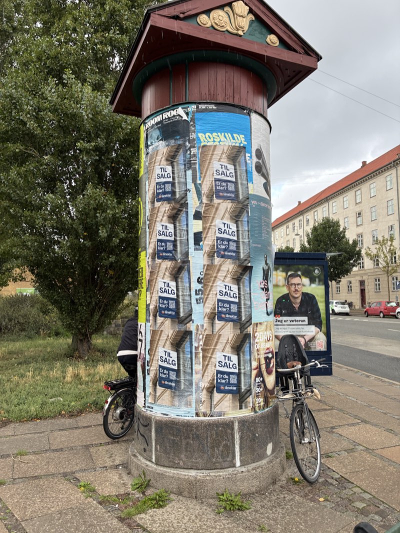 En plakatsøjle med rødt tag og Låneklars plakater
